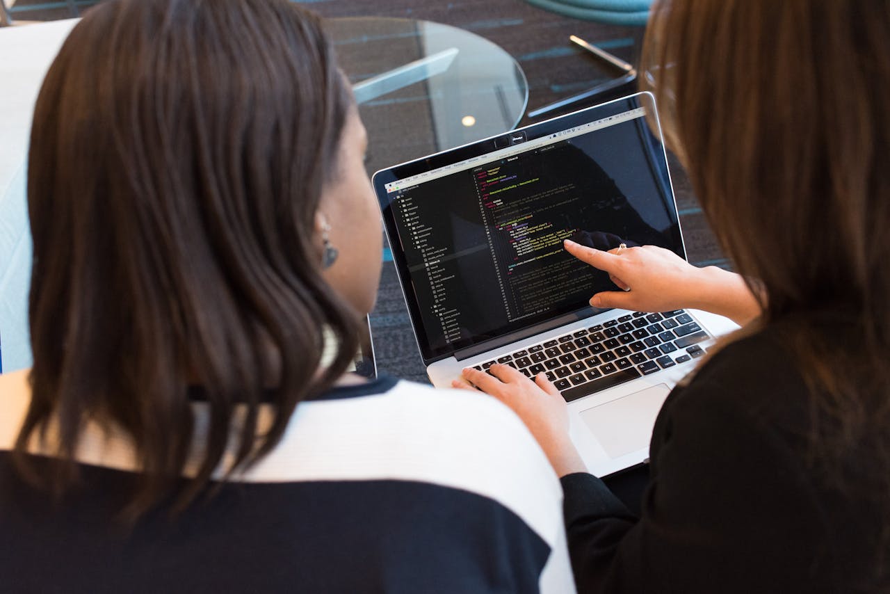 service-04 Two women working together on software programming indoors, focusing on code.